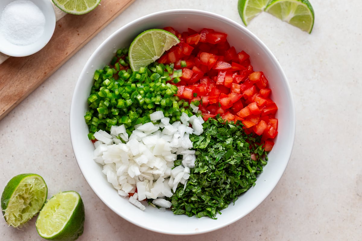 ingredients for pico de gallo sectioned out in a large bowl including tomatoes, jalapeno, cilantro, onion, and lime