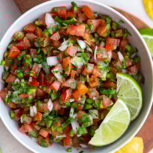 pico de gallo in a white bowl with 2 limes on top
