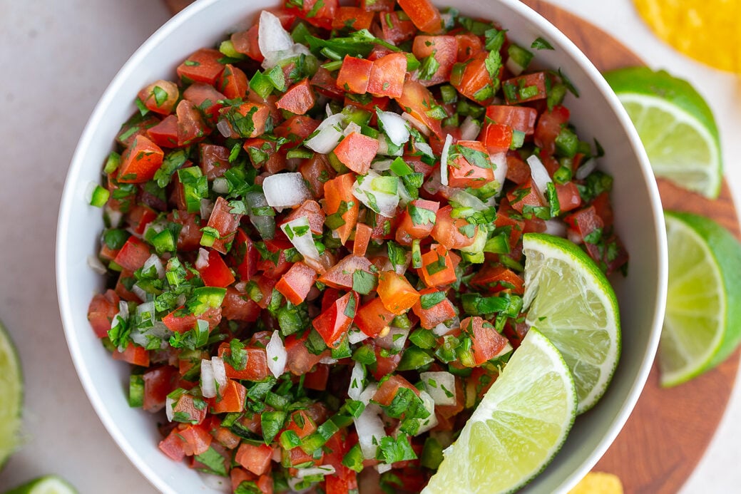 pico de gallo in a white bowl with 2 limes on top