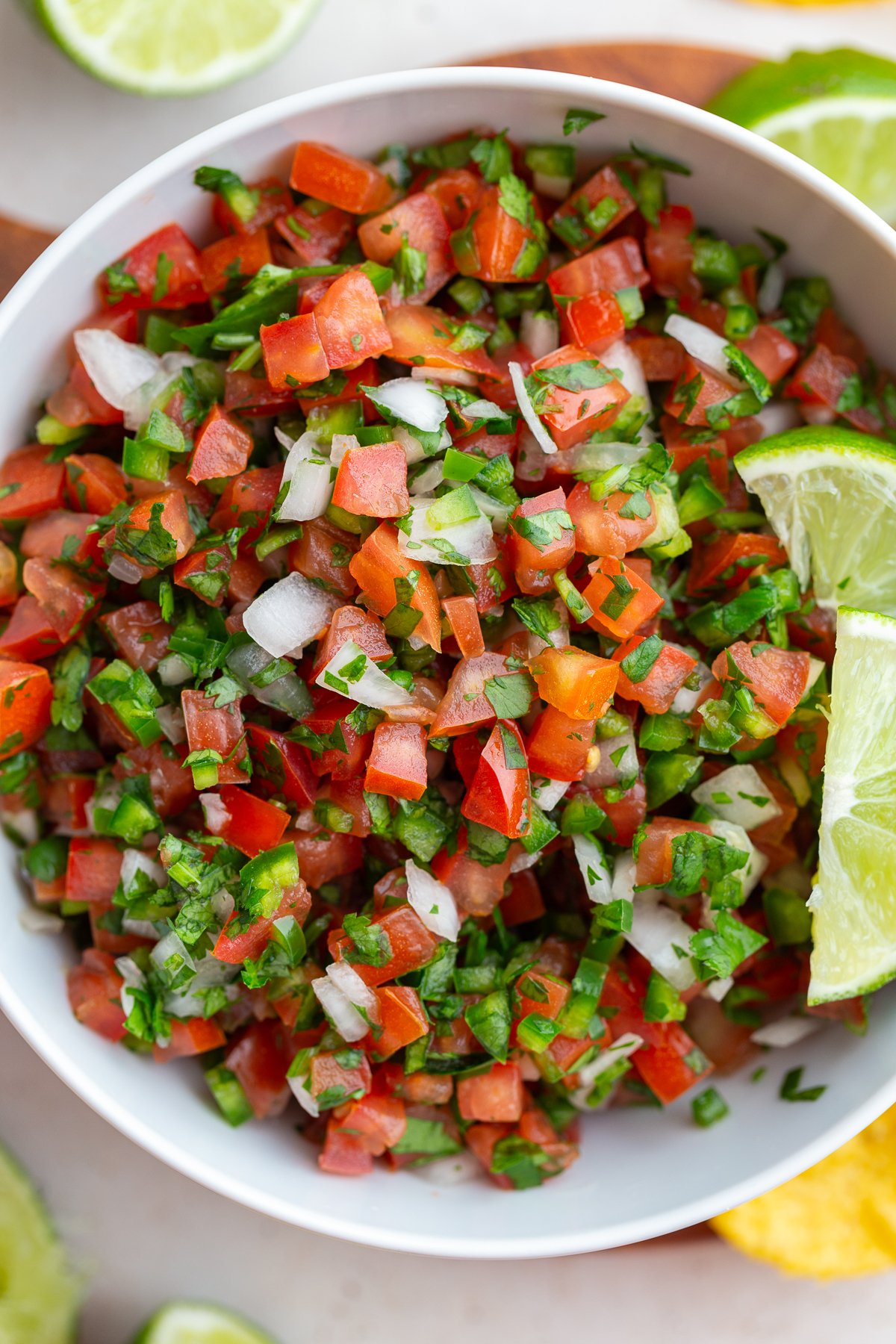 pico de gallo in a white bowl with 2 limes on top