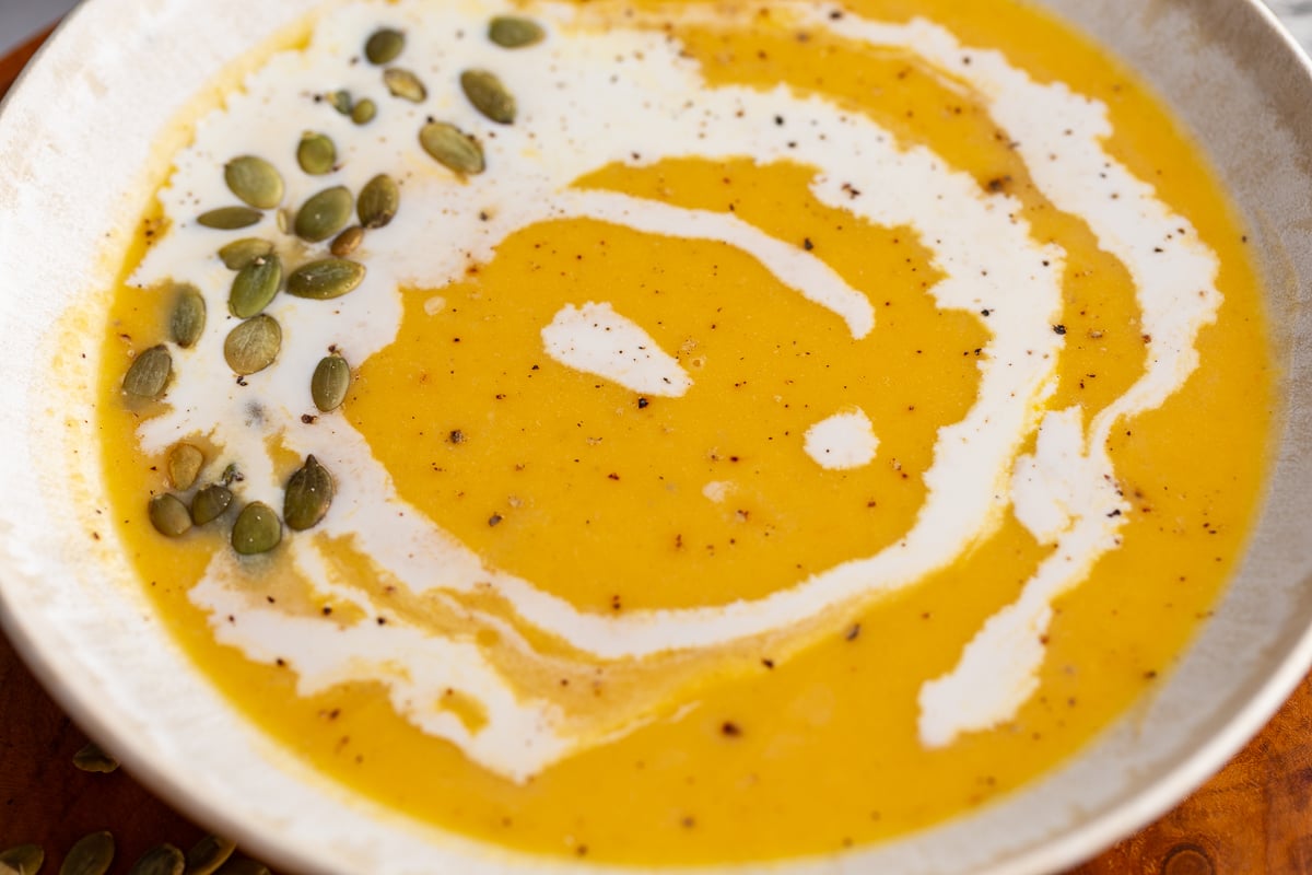 Creamy Roasted Butternut Squash Soup in a large bowl drizzled with cream and pepitas