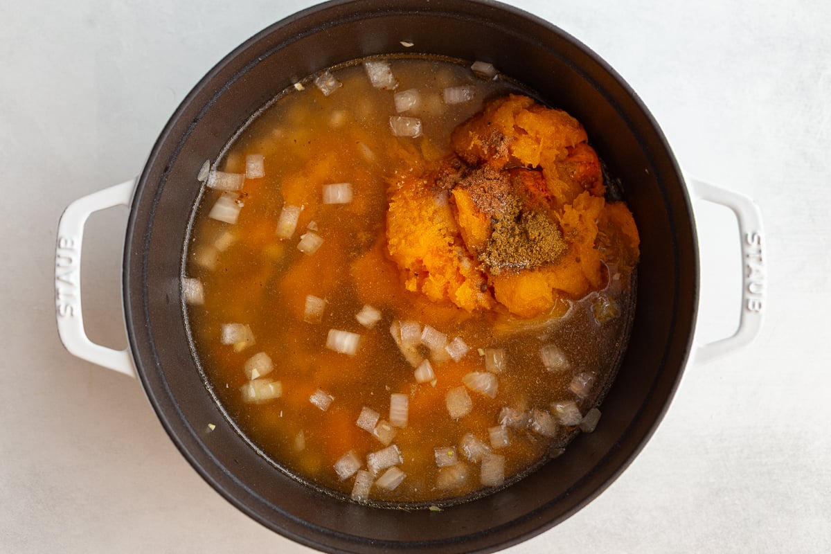 butternut squash soup in a pot before it's been blended. you can see the onions and chunks of squash floating in the pot of broth