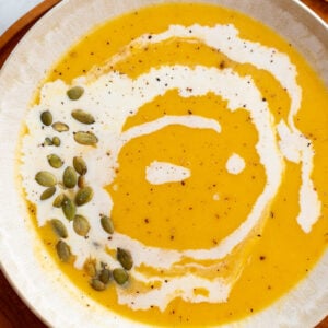 Creamy Roasted Butternut Squash Soup in a large bowl drizzled with cream and pepitas