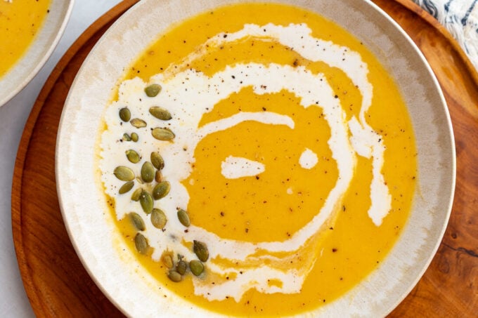 Creamy Roasted Butternut Squash Soup in a large bowl drizzled with cream and pepitas