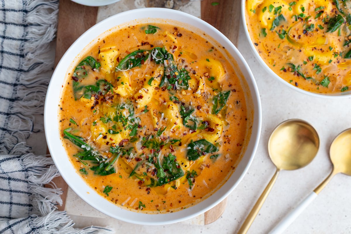 Creamy tortellini soup and greens in a white bowl