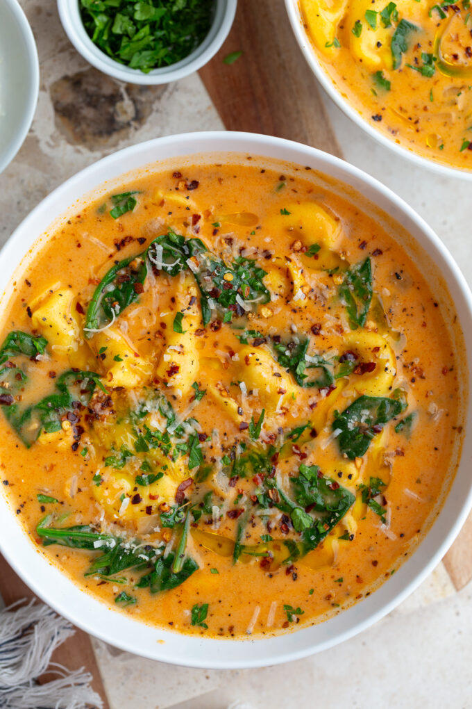 Creamy tortellini soup and greens in a white bowl