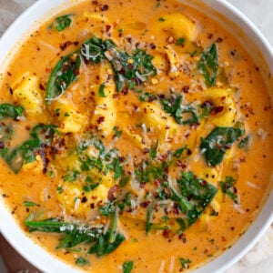 Creamy tortellini soup and greens in a white bowl