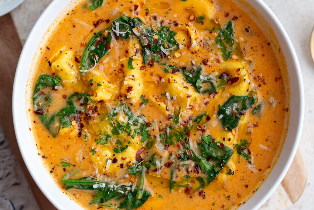 Creamy tortellini soup and greens in a white bowl