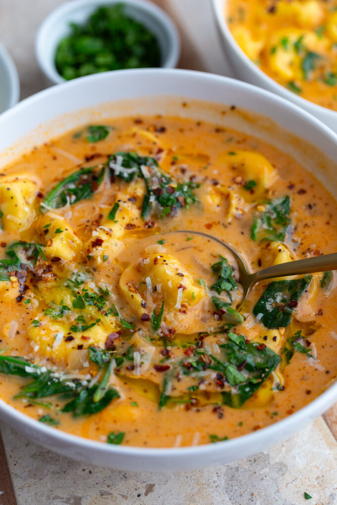 vegetarian tortellini soup in a large bowl with a spoon scooping in