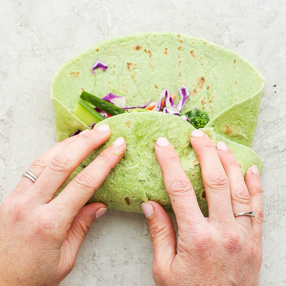 hands folding up a green spinach wrap