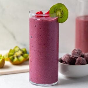 acai smoothie in a tall glass topped with raspberry and kiwi with more kiwi in the background