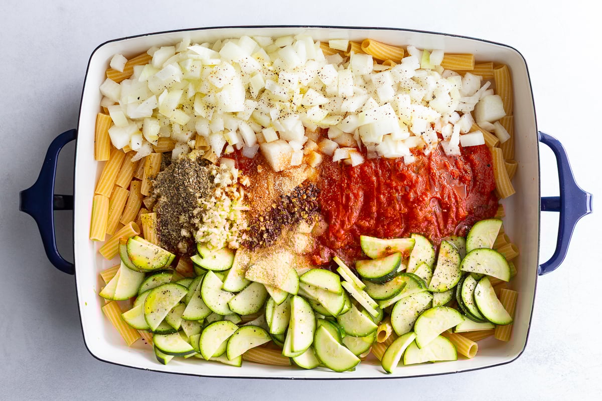 dump and bake ingredients in a pan for baked pasta including rigatoni, marinara, zucchini, onion and spices
