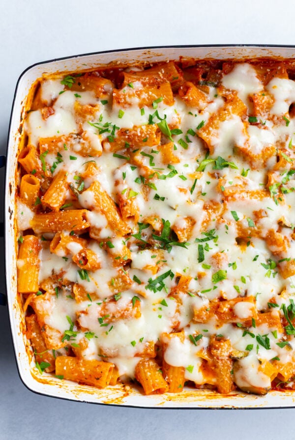 baked rigatoni pasta that's topped with melted cheese and fresh green herbs