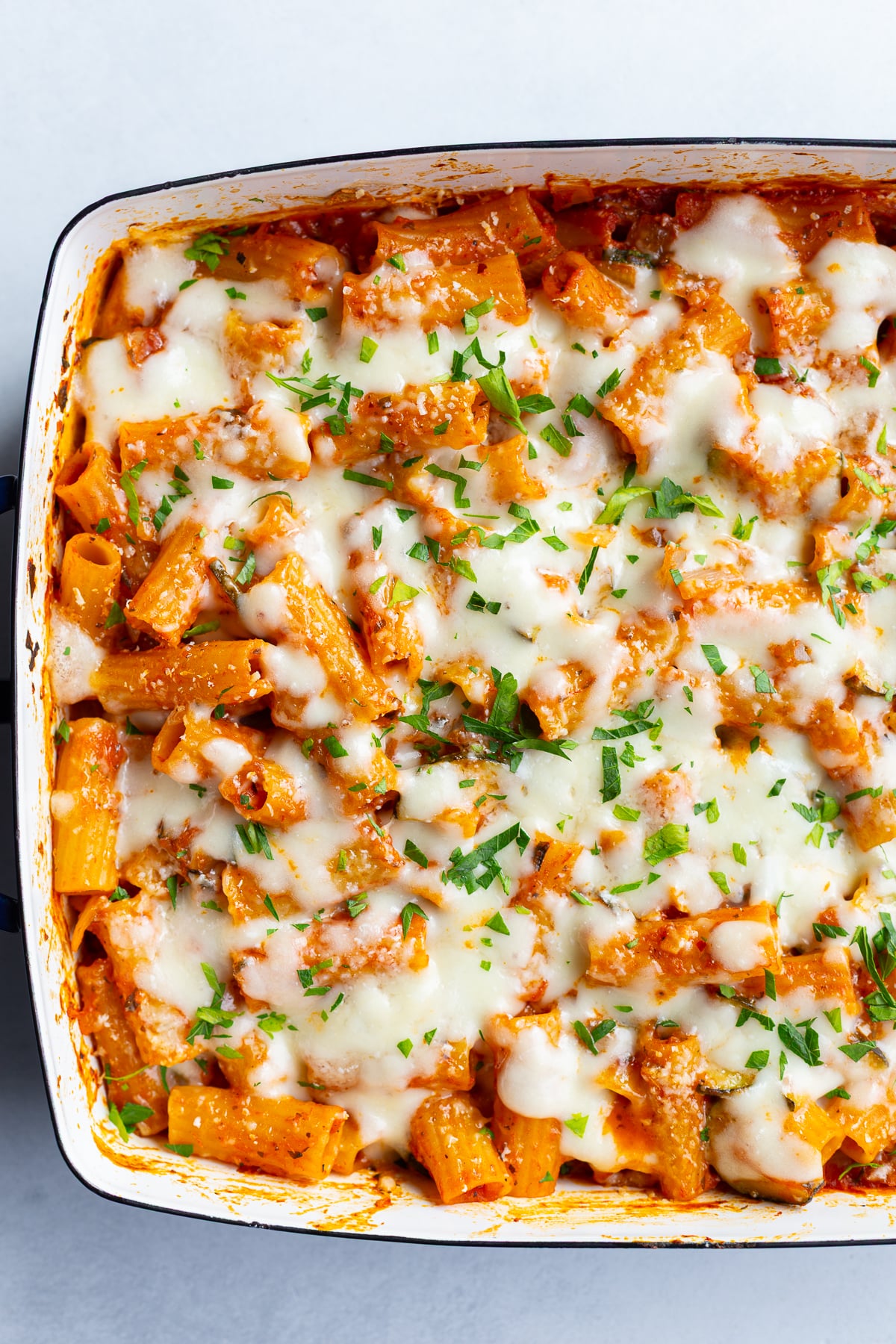 baked rigatoni pasta that's topped with melted cheese and fresh green herbs