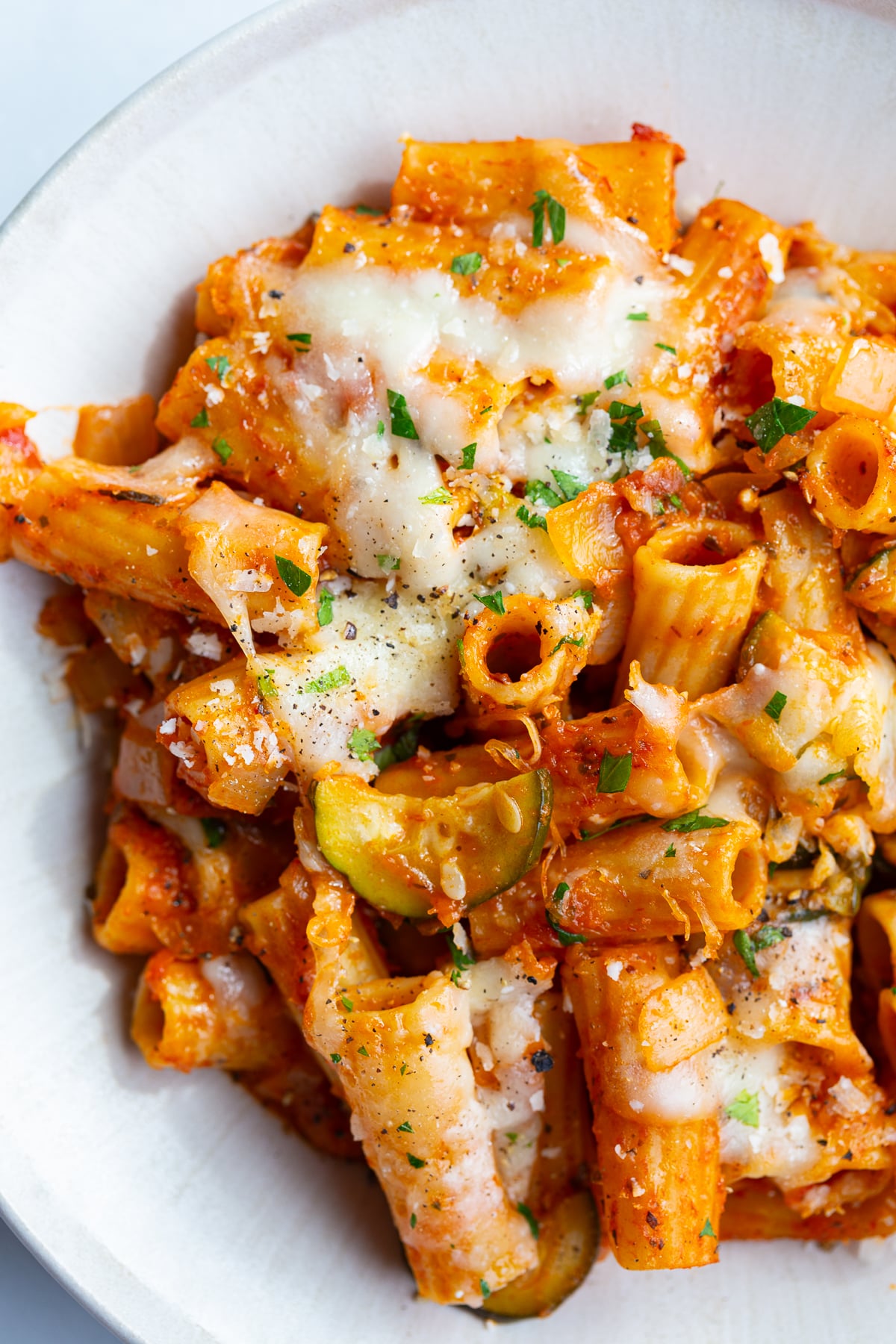 baked rigatoni pasta that's topped with melted cheese and fresh green herbs