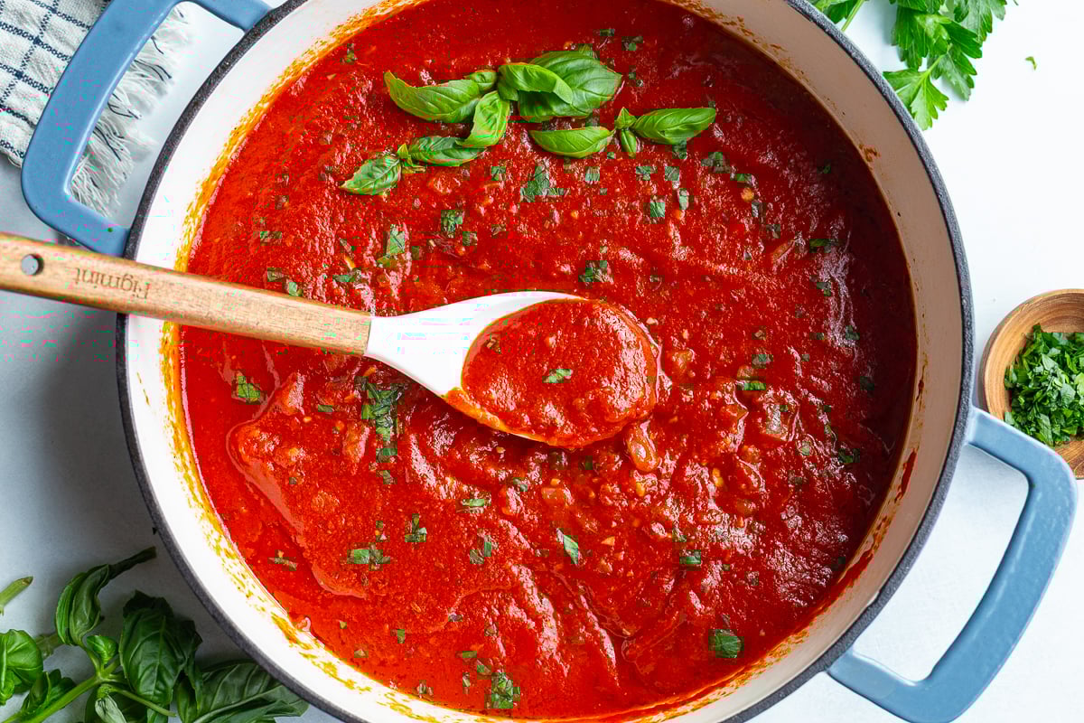 quick marinara sauce in a large skillet. there's green basil on top and a spoon in the pot with some sauce scooped up