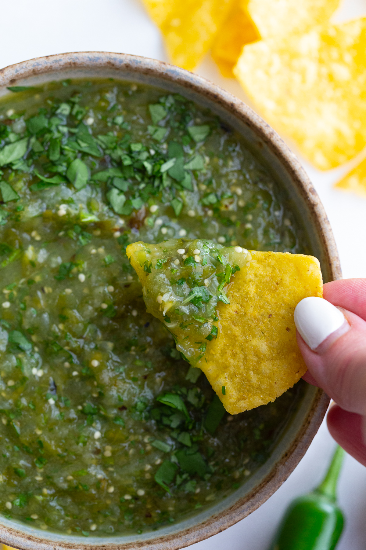 salsa verde in a bowl with a hand holding a tortilla chip dipping into the salsa