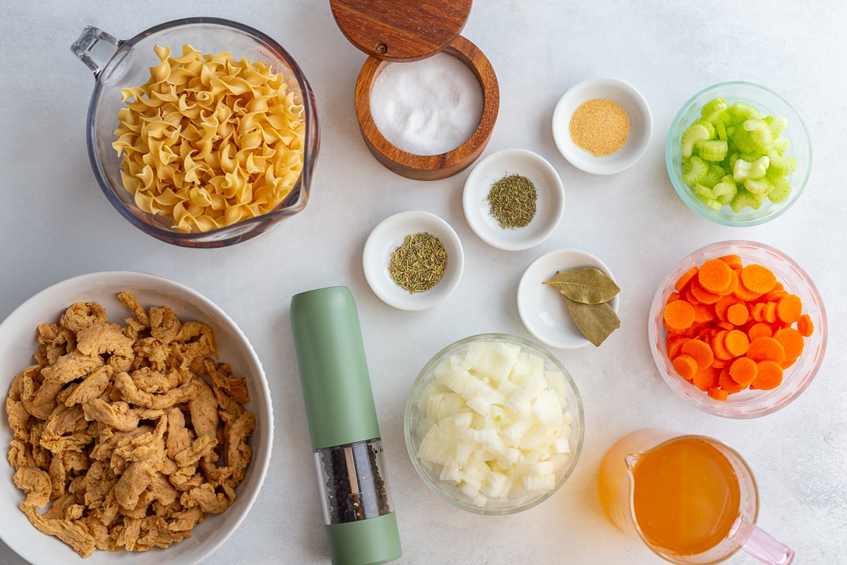 ingredients needed for vegetarian chicken noodle soup including egg noodles, onion, soy curls, salt and pepper, broth, celery and carrots