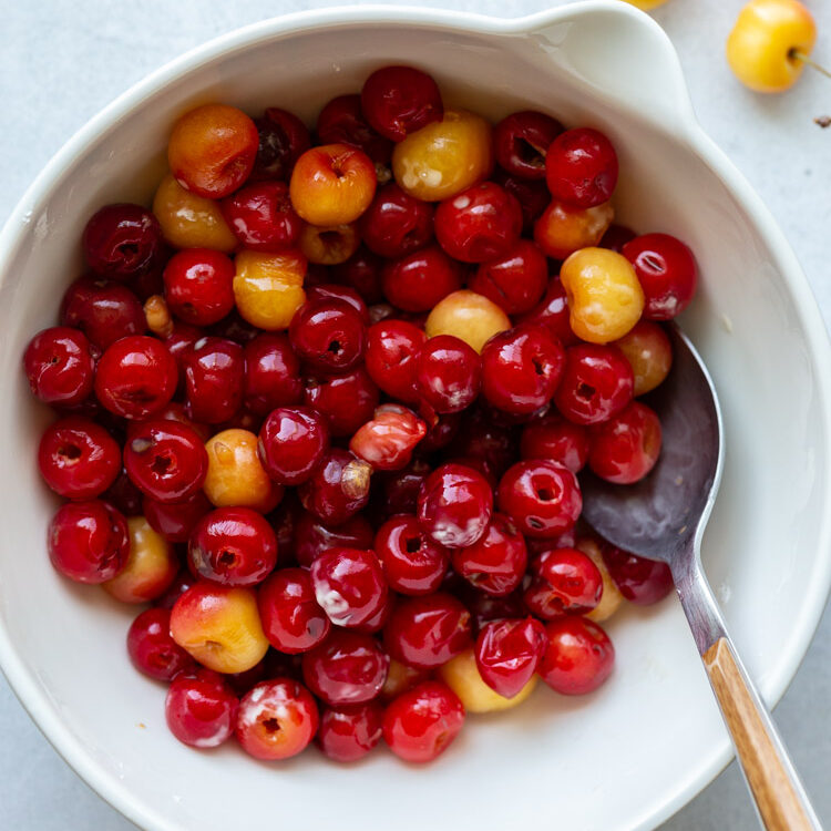 tossing cherries with maple syrup in a white mixing bowl