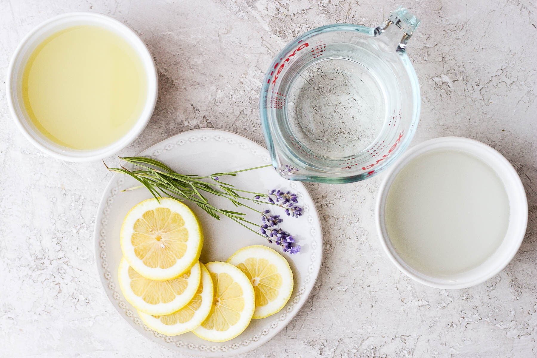 ingredients for lavender lemonade on a white board: fresh lemons and lavender, lemon juice, water, and simple syrup