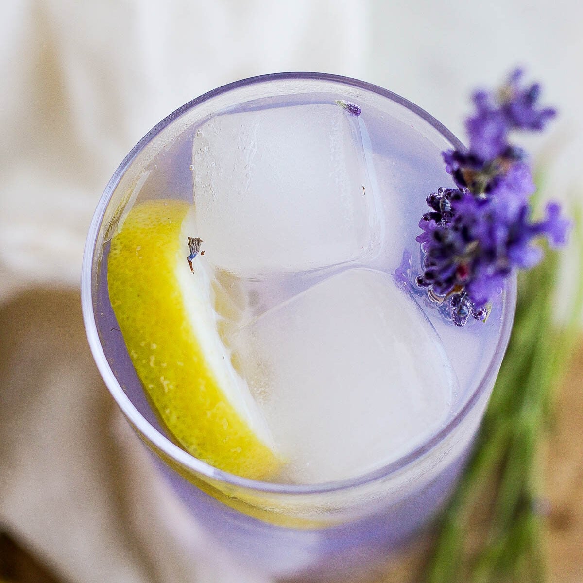 lavender lemonade in a tall glass with ice and fresh lavender plus lemon slices in the glass