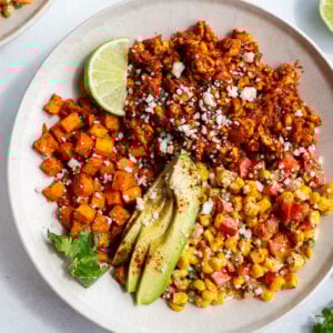street corn tofu bowls with roasted sweet potato, ground tofu "meat", sliced avocado, lime wedge, and street corn salad in a bowl