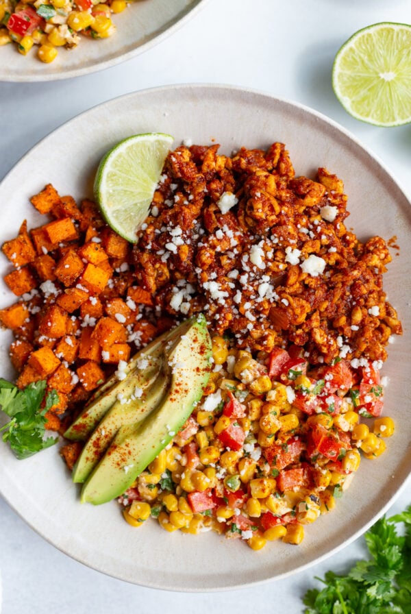 street corn tofu bowls with roasted sweet potato, ground tofu "meat", sliced avocado, lime wedge, and street corn salad in a bowl