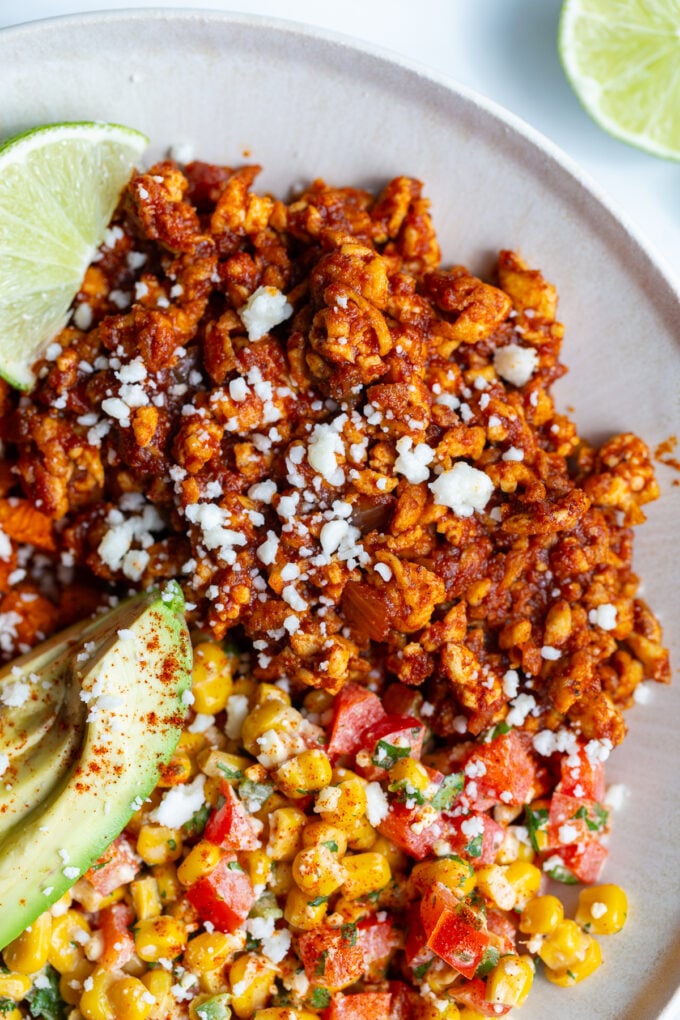 street corn tofu bowls with roasted sweet potato, ground tofu "meat", sliced avocado, lime wedge, and street corn salad in a bowl