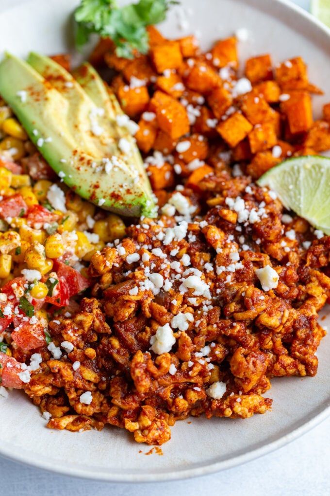 street corn tofu bowls with roasted sweet potato, ground tofu "meat", sliced avocado, lime wedge, and street corn salad in a bowl