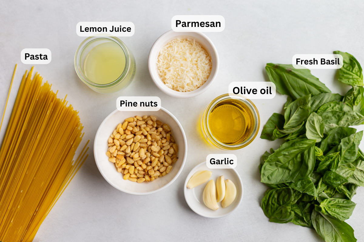 ingredients needed to make homemade pesto pasta including pasta, garlic, lemon, pine nuts, and basil