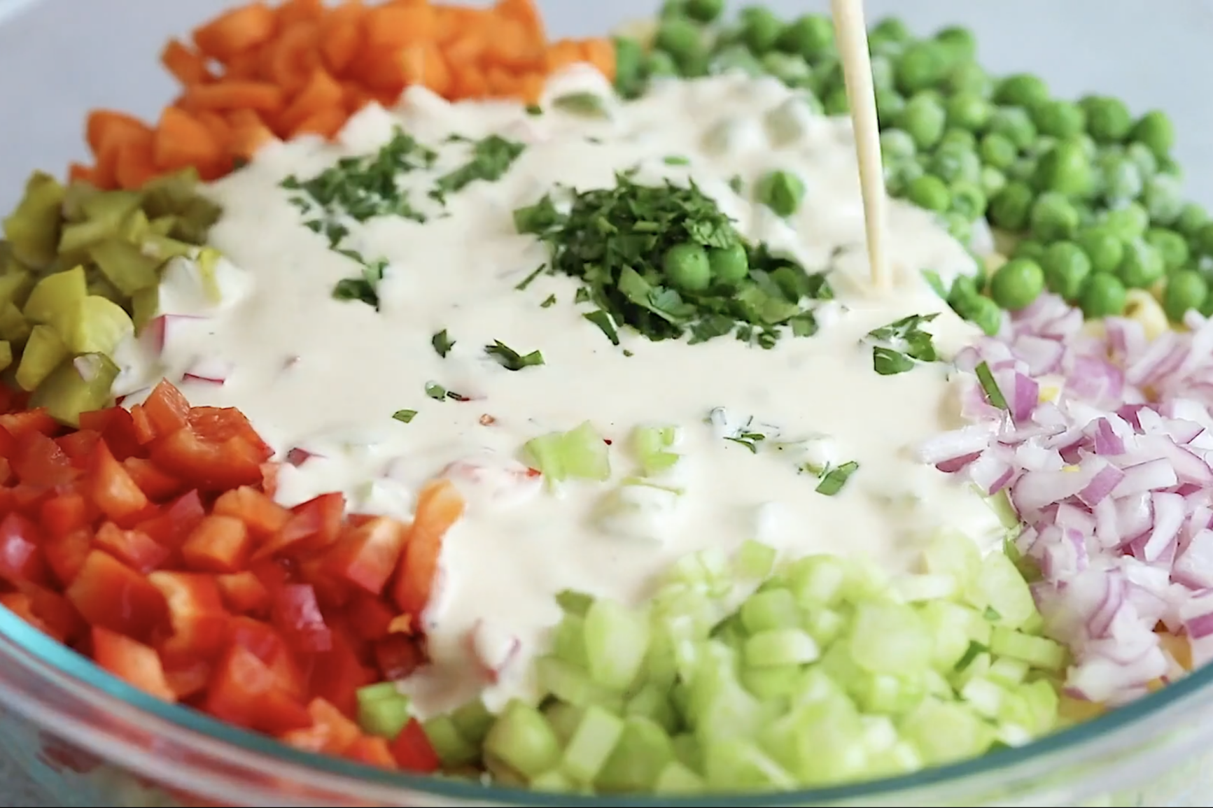 dressing being poured on top of macaroni and veggies to make a macaroni salad