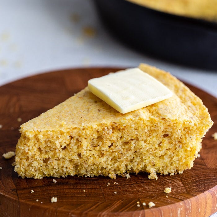 slice of cornbread on a wood board with a slice of butter on top