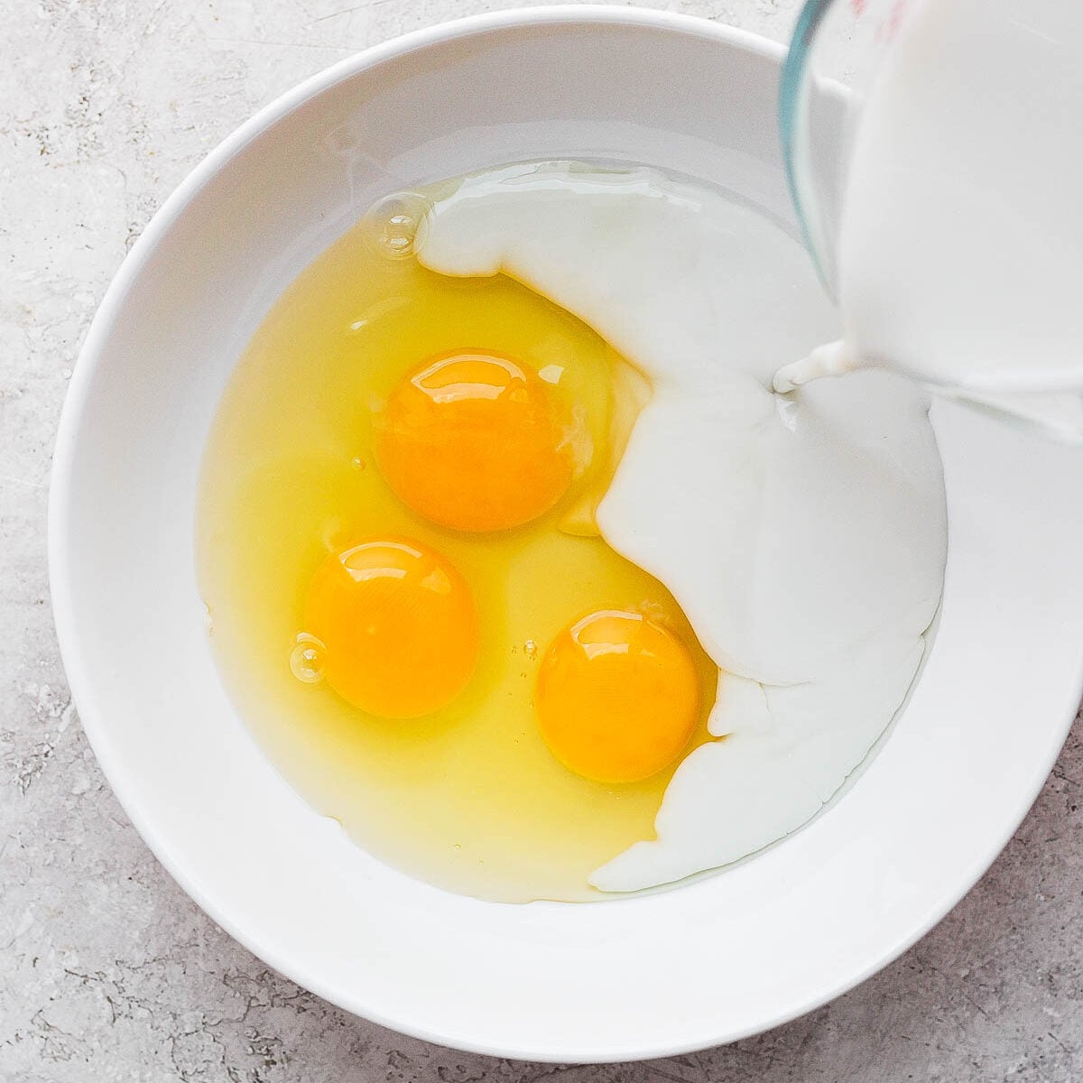 Pouring milk in a bowl with three eggs.