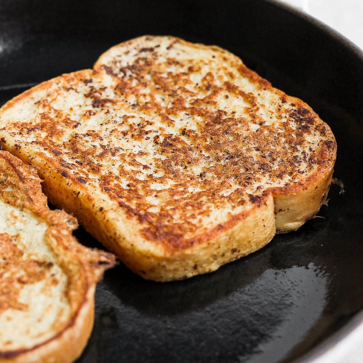 Slice of French toast cooking in a pan.