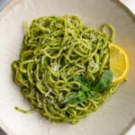 pesto pasta on a plate with a lemon wedge and fresh basil