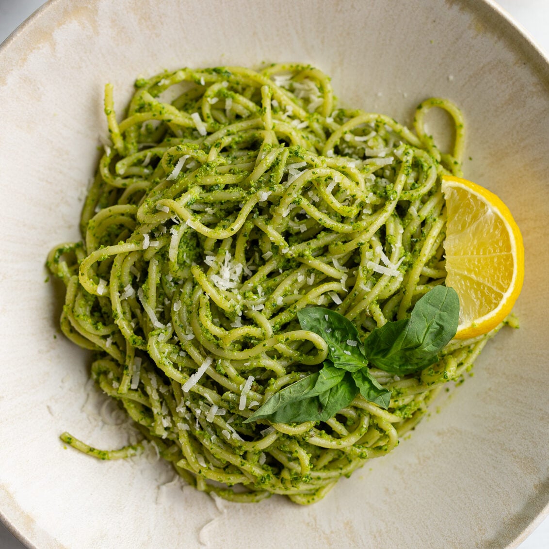 pesto pasta on a plate with a lemon wedge and fresh basil