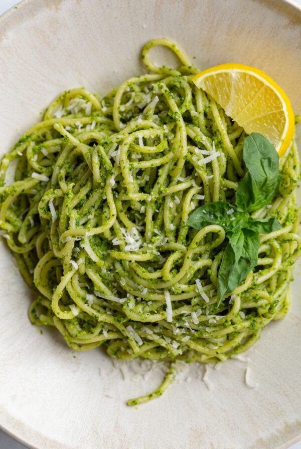 pesto pasta on a plate with a lemon wedge and fresh basil