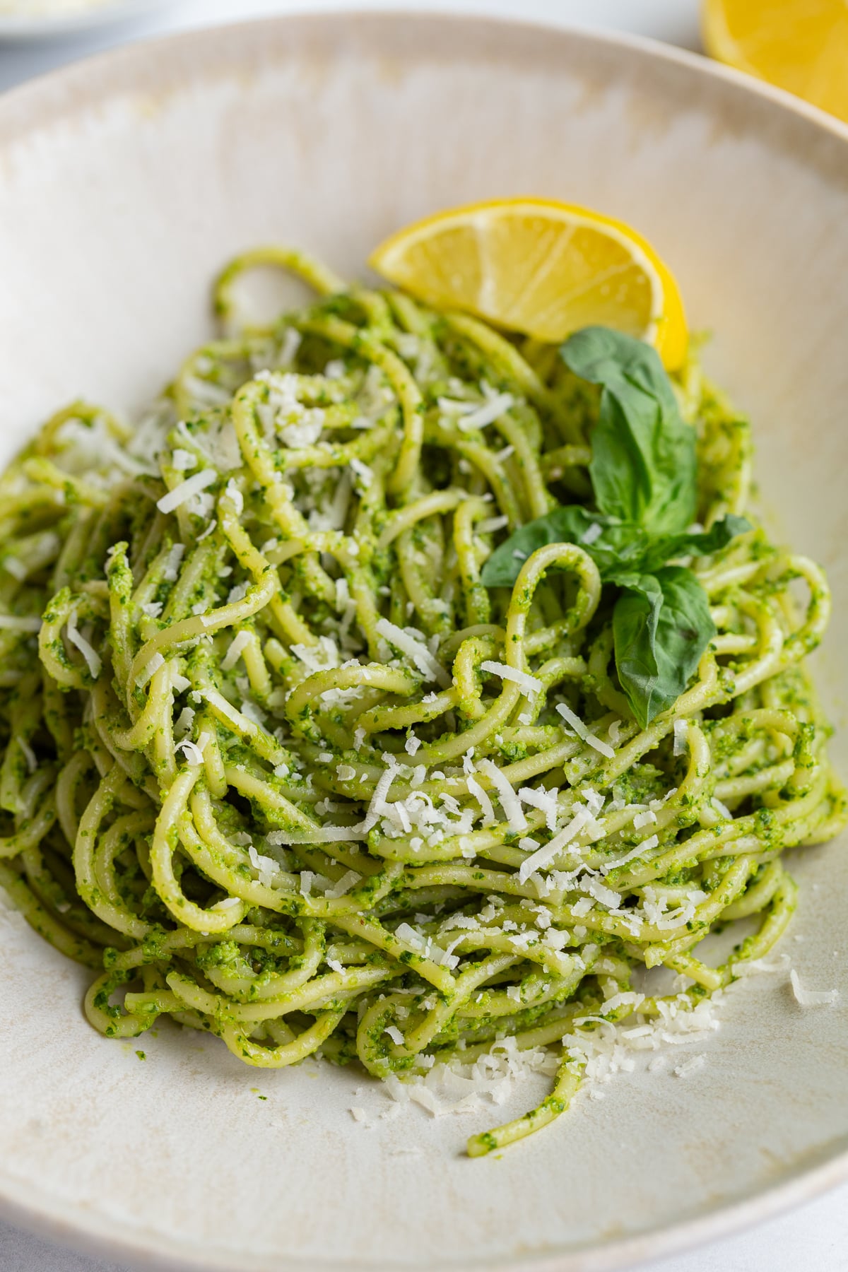 pesto pasta on a plate with a lemon wedge and fresh basil