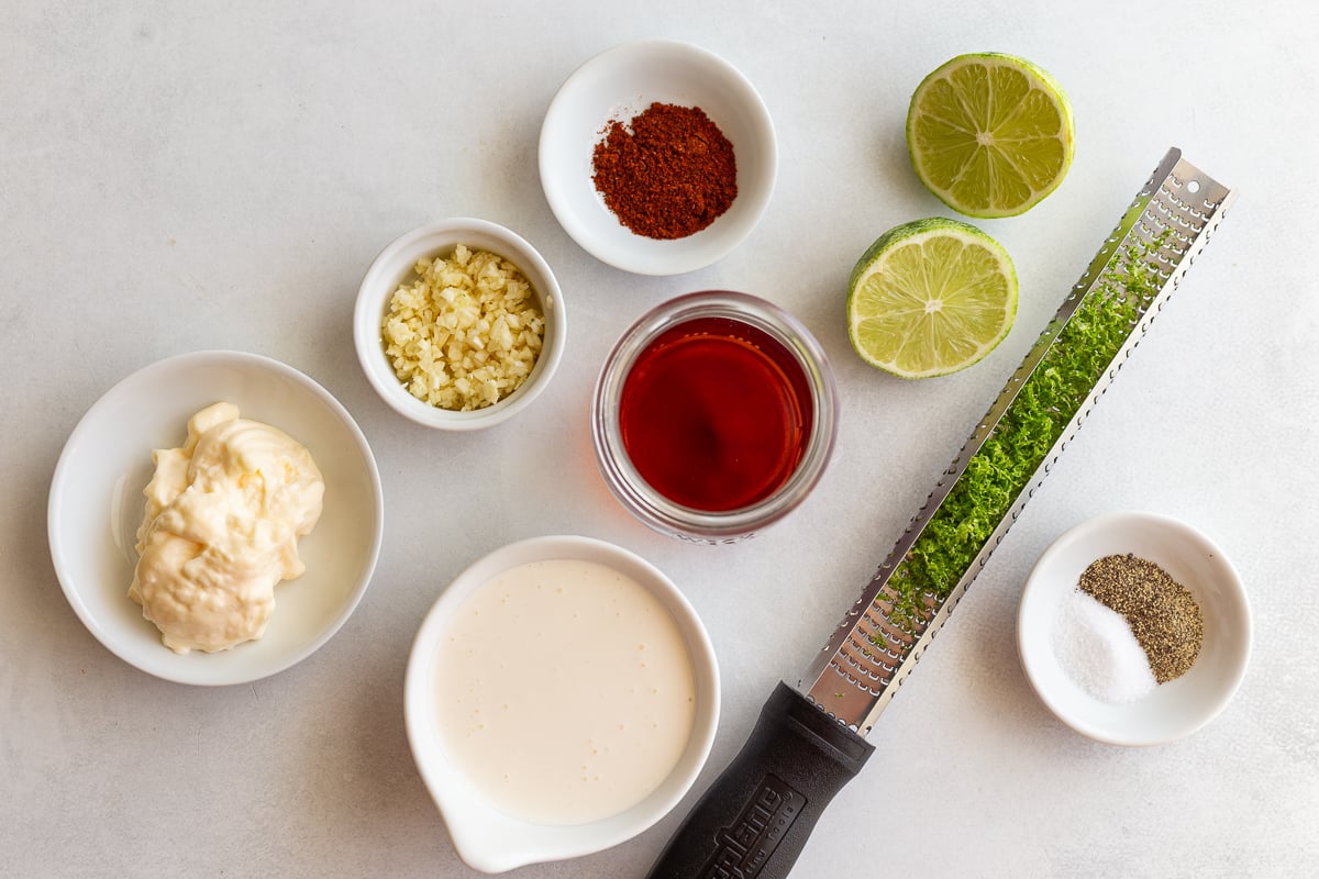ingredients laid out that are needed to make a street corn dressing including sour cream, mayo, lime juice and zest, chili powder, and garlic