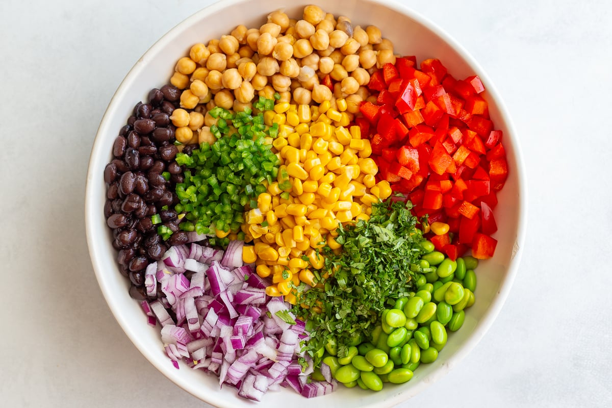 street corn salad veggies in a large bowl for dense beans salad including corn, beans, cilantro, jalapeno, red onion, and edamame