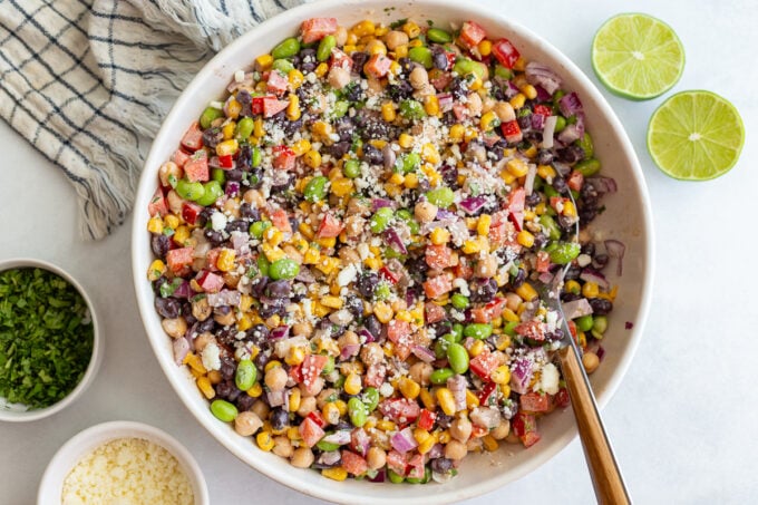 mexican street corn dense bean salad in a large bowl filled with chickpeas, pinto beans, edamame, and fresh veggies topped with cotija