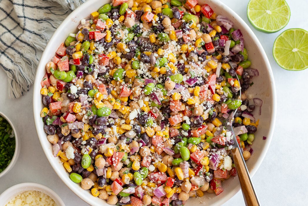 mexican street corn dense bean salad in a large bowl filled with chickpeas, pinto beans, edamame, and fresh veggies topped with cotija