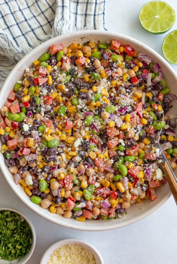 mexican street corn dense bean salad in a large bowl filled with chickpeas, pinto beans, edamame, and fresh veggies topped with cotija