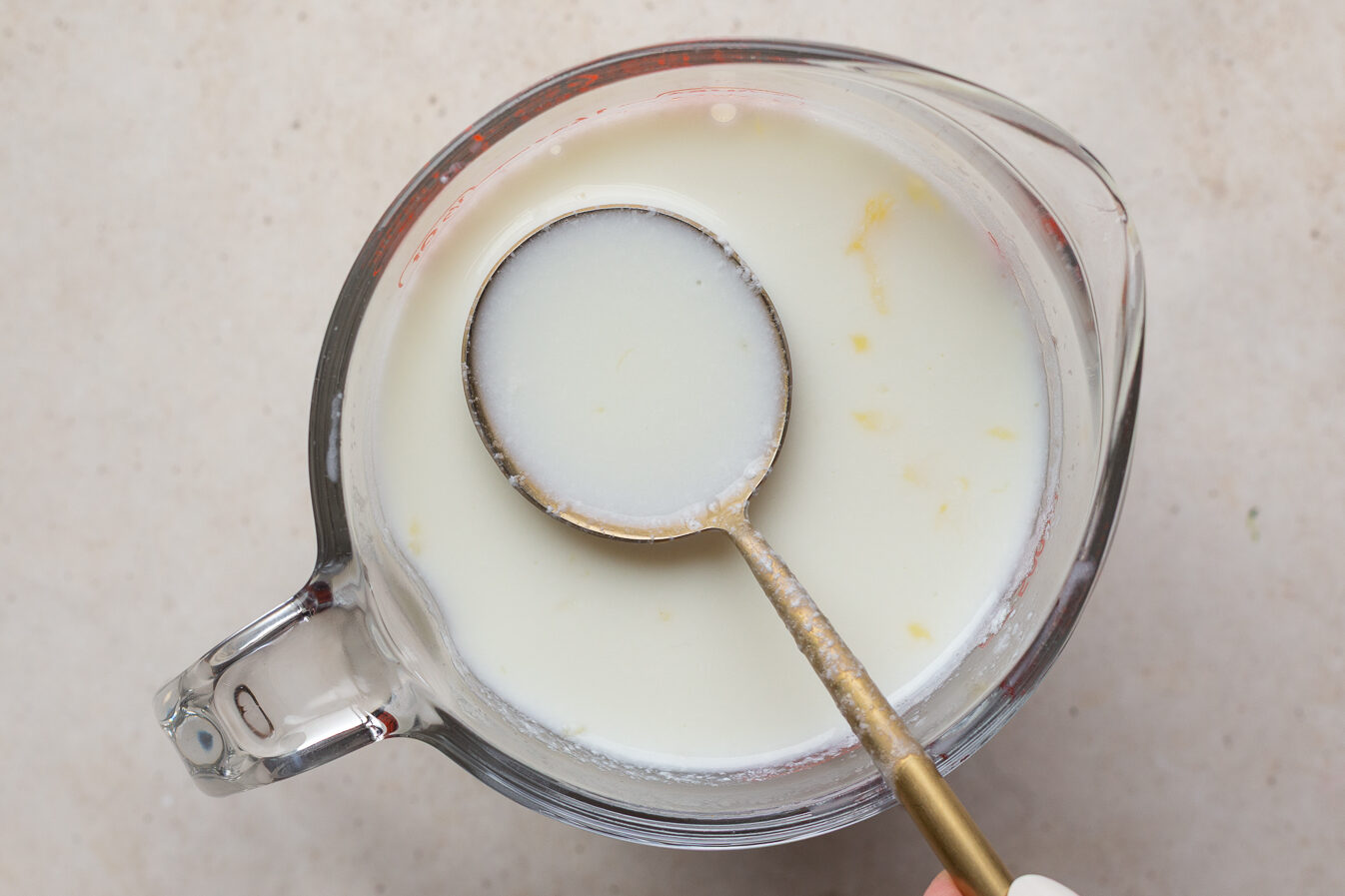 Using a spoon to stir milk and lemon juice in a spouted measuring glass.