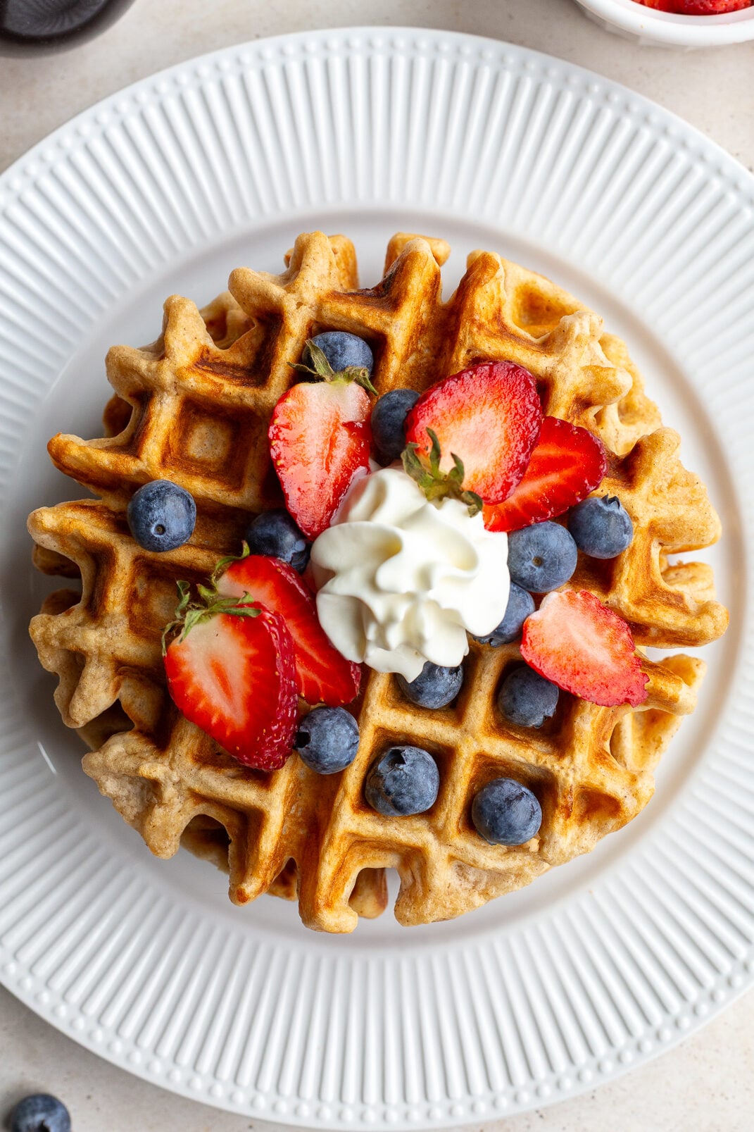 Waffle on a white plate topped with berries and whipped cream.