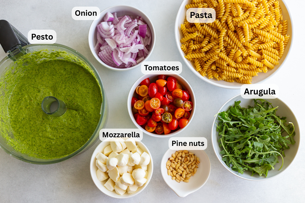 ingredients needed for pesto pasta salad including pasta, pesto, tomatoes, mozzarella and red onion