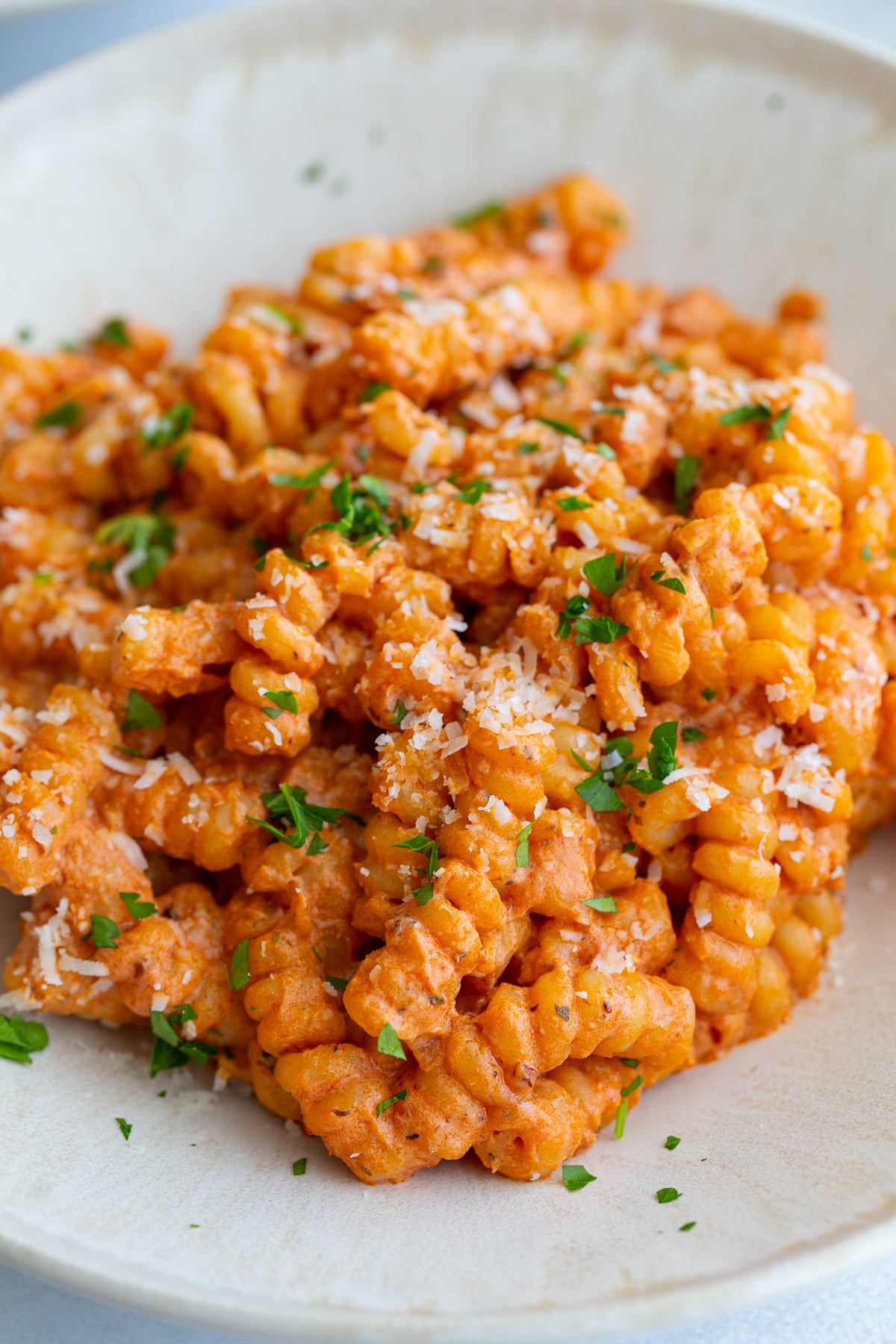 creamy tomato protein pasta in a pasta bowl and topped with herbs