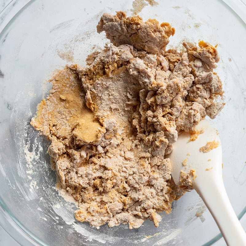 Using a spatula to stir flour with pumpkin in a large bowl.