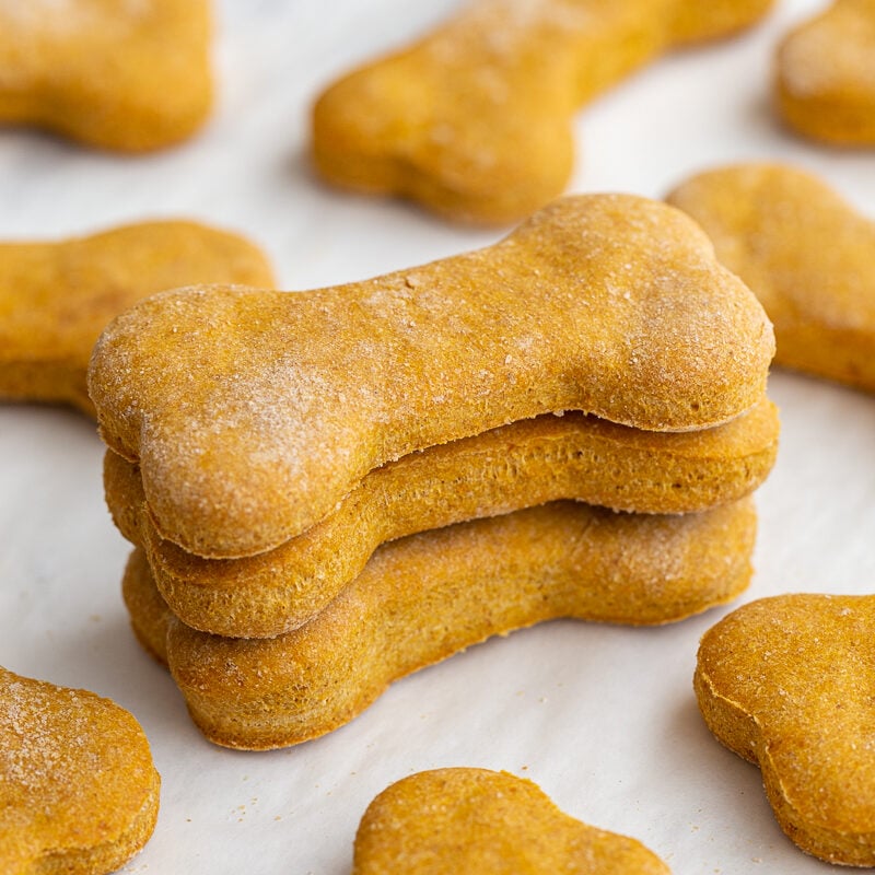Three pumpkin dog biscuits shaped like bones stacked. 