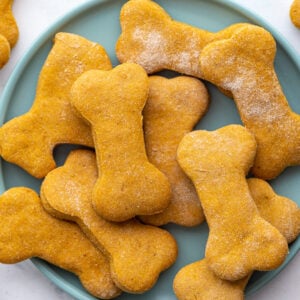 Pumpkin dog biscuits shaped like dog bones on a plate.